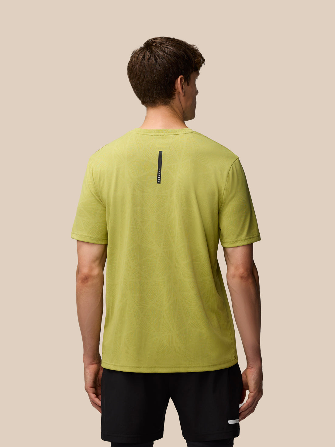 Back view of a man wearing Flow Training Engineered Knit T Shirt in mustard with a vertical Castore stripe on the upper back.