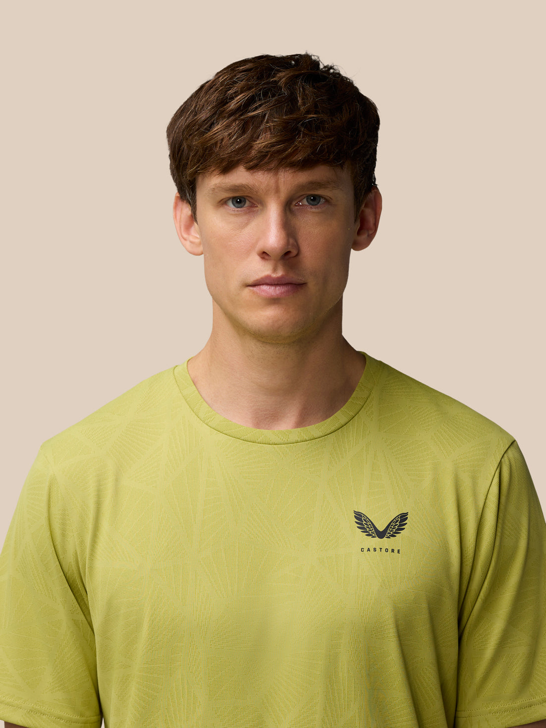 Close up of a male model wearing Flow Training Engineered Knit T Shirt in mustard, showcasing knit pattern and Castore logo.