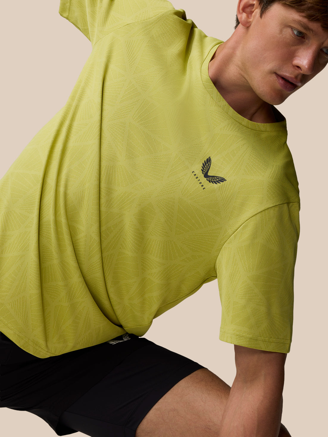 Male model wearing Flow Training Engineered Knit T Shirt in mustard with geometric knit pattern and Castore logo on chest.