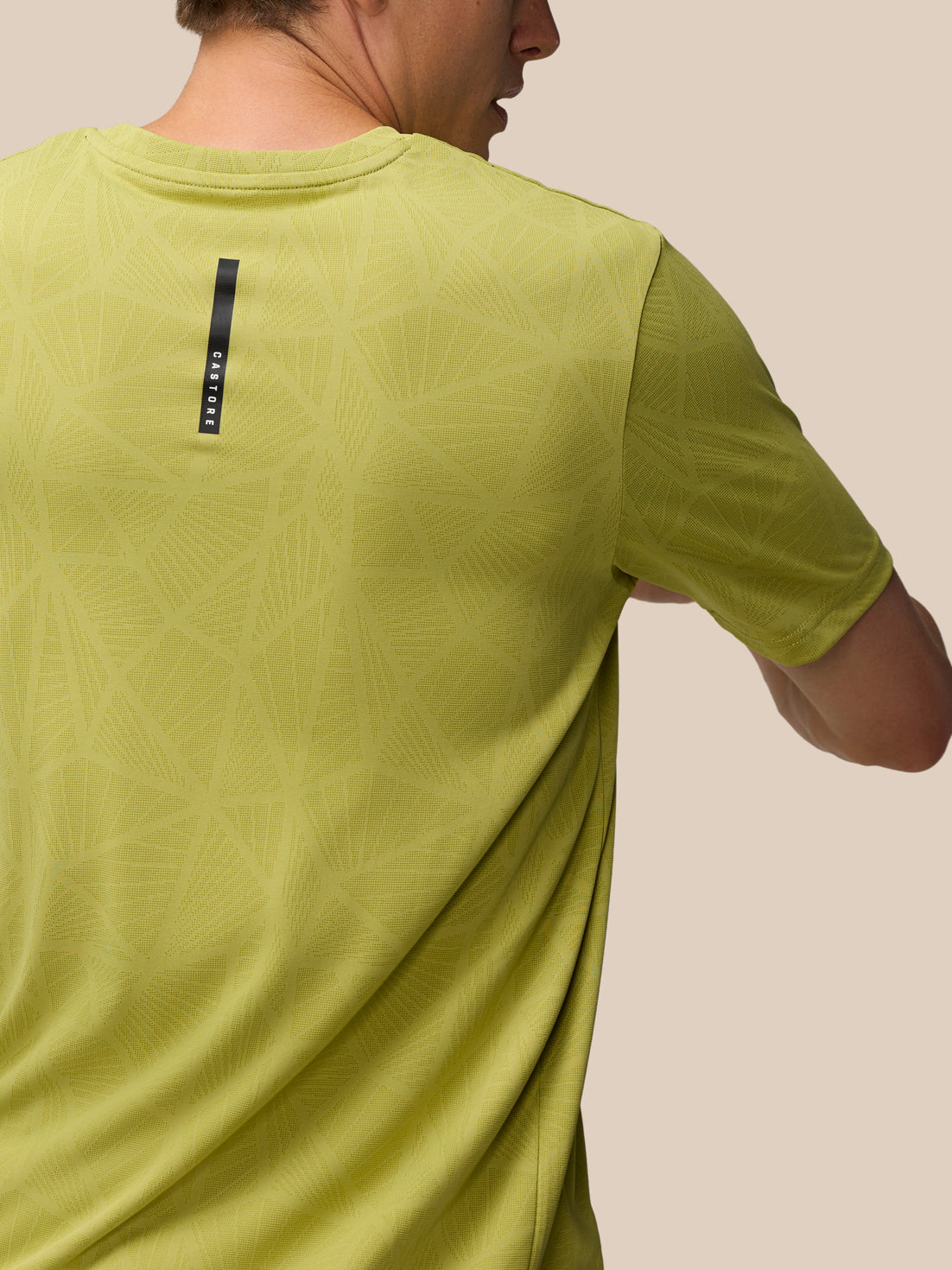 Close-up of the back of mustard Flow Engineered Knit T Shirt showing the geometric knit pattern and a vertical Castore tag.