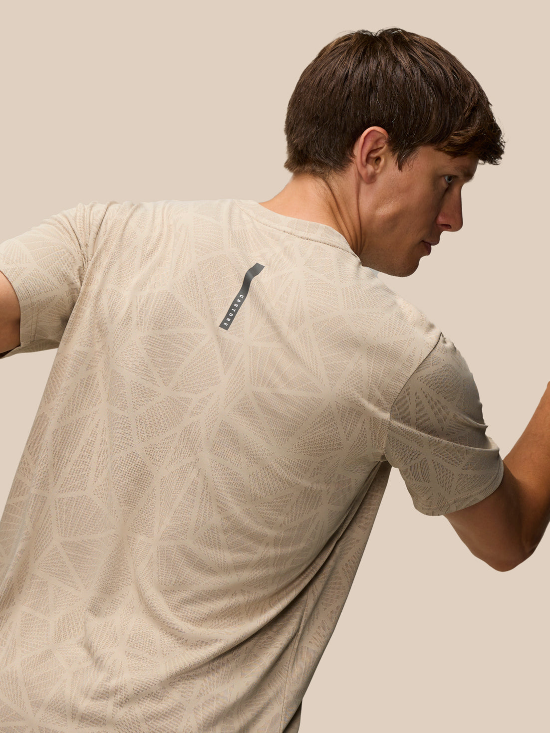 Back view of a man wearing Flow Engineered Knit T Shirt in mushroom with a geometric knit pattern and a vertical Castore label on the upper back