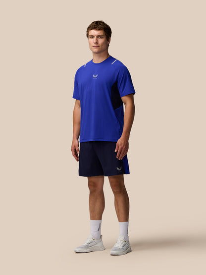 Full body shot of a man in azure blue Apex Training T Shirt with mesh side panel and Castore logo on the chest