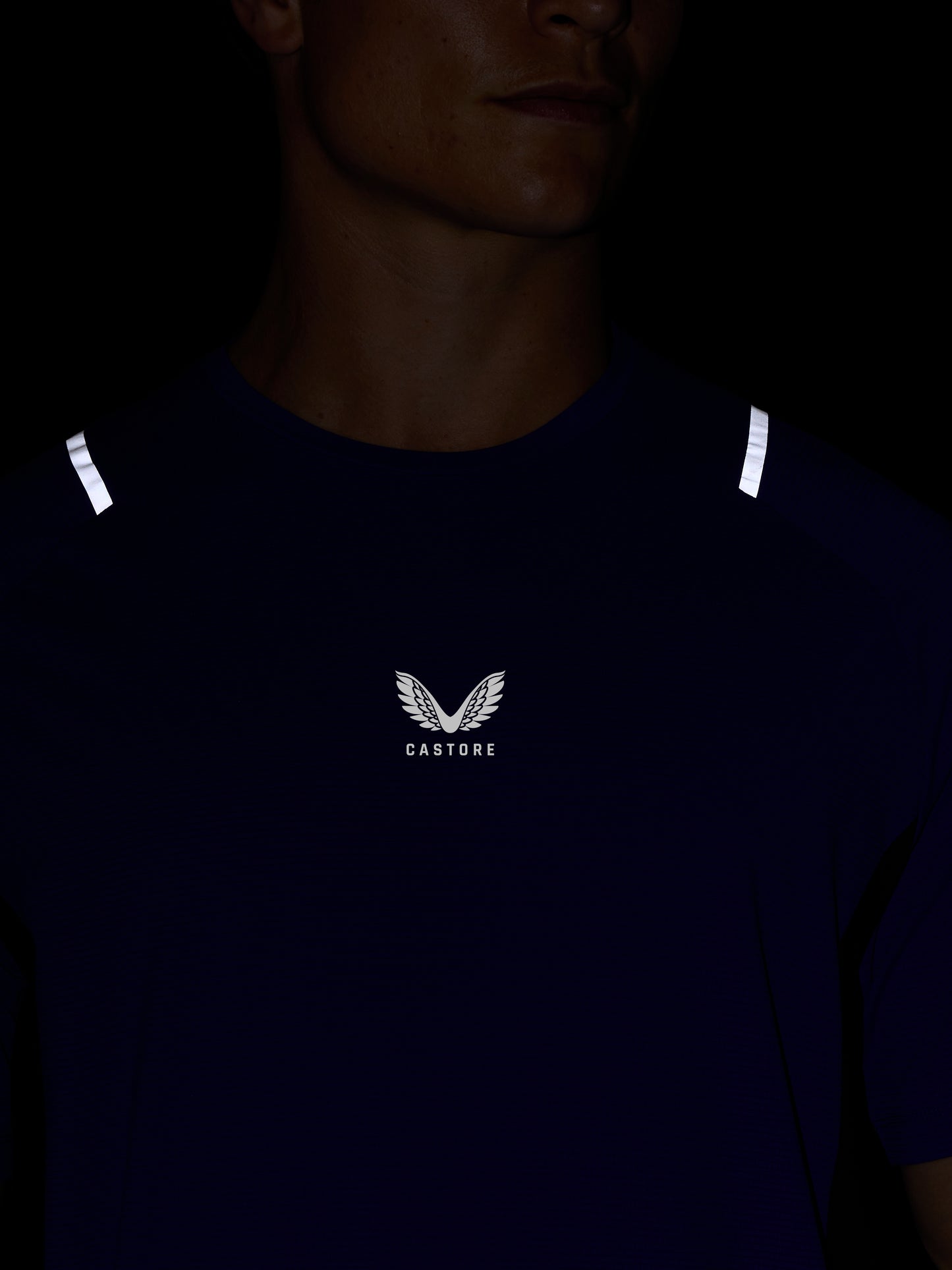 Close-up of Azure blue Apex Training T-Shirt worn by a model, featuring white reflective shoulder accents and the Castore logo on the chest.