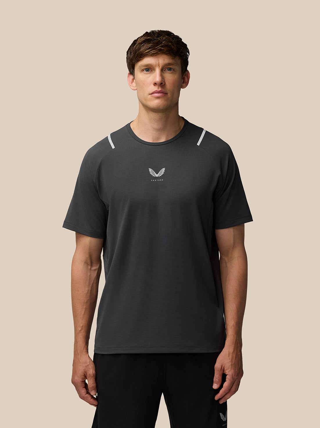 Man wearing gunmetal Apex Training T Shirt with reflective shoulder hits and Castore logo at center chest.
