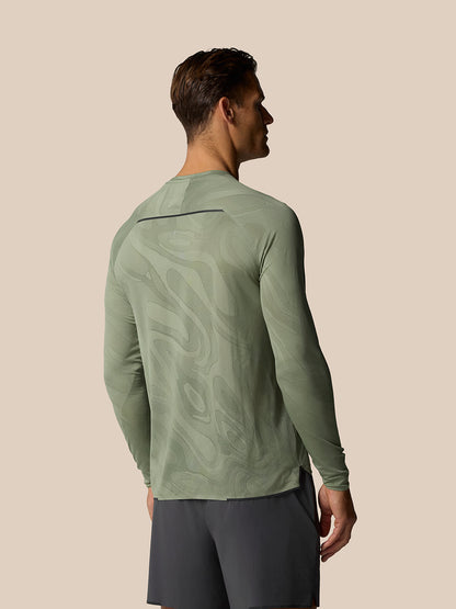 Back view of a man wearing Zone Training LVS Long Sleeve Top Thyme, showing abstract pattern and back ventilation detail.