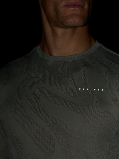 Close-up of a man wearing a dark patterned Zone Training LVS Long Sleeve Top in Thyme with a round neckline and a Castore logo on the chest