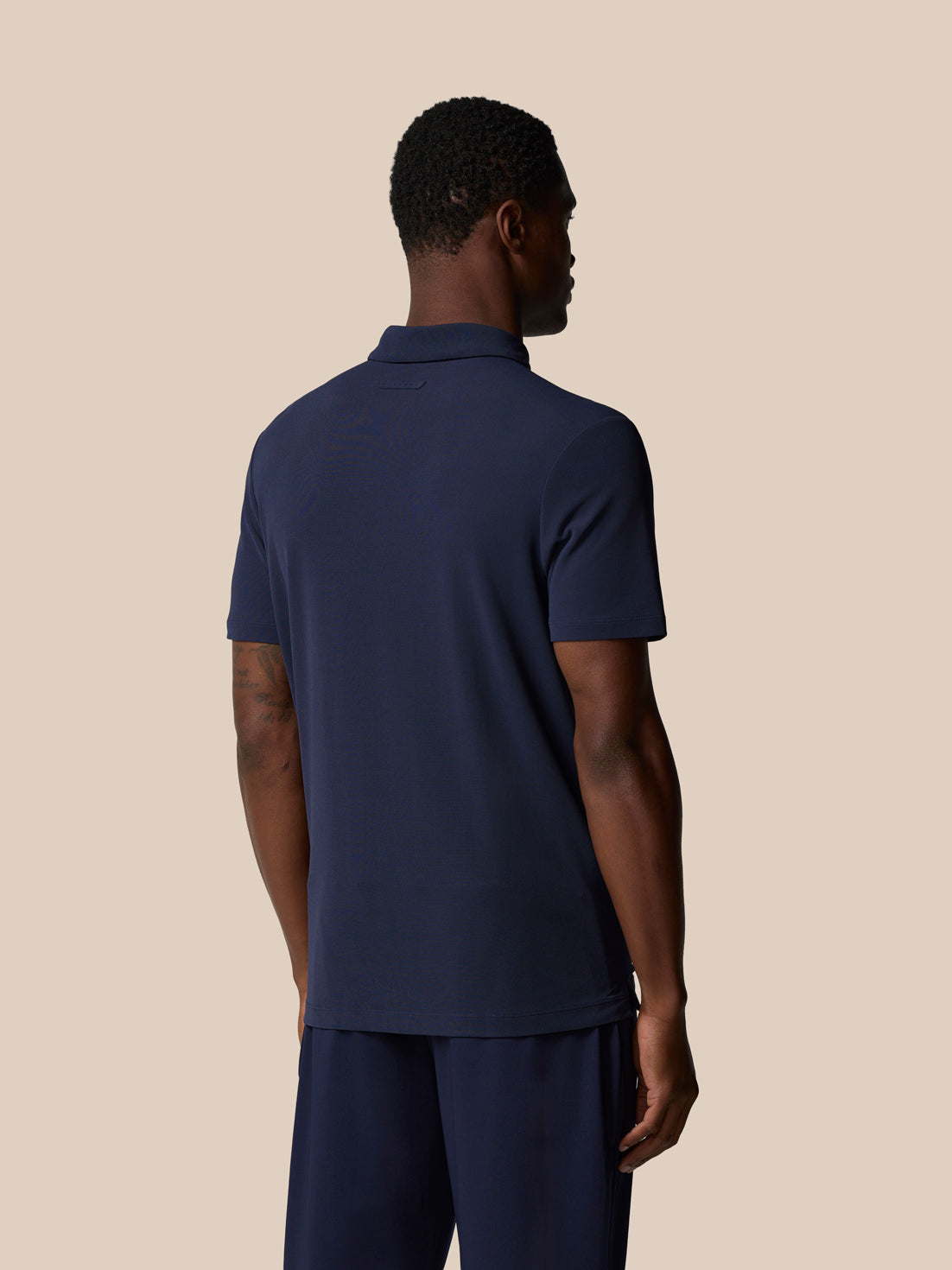 Back view of male model wearing navy Elevated Lifestyle Polo highlighting back neck tape.
