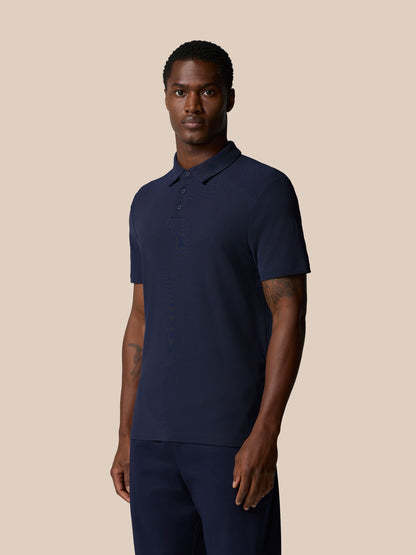 Rear three-quarter view of male model wearing navy Elevated Lifestyle Polo showing back neck area and badge.