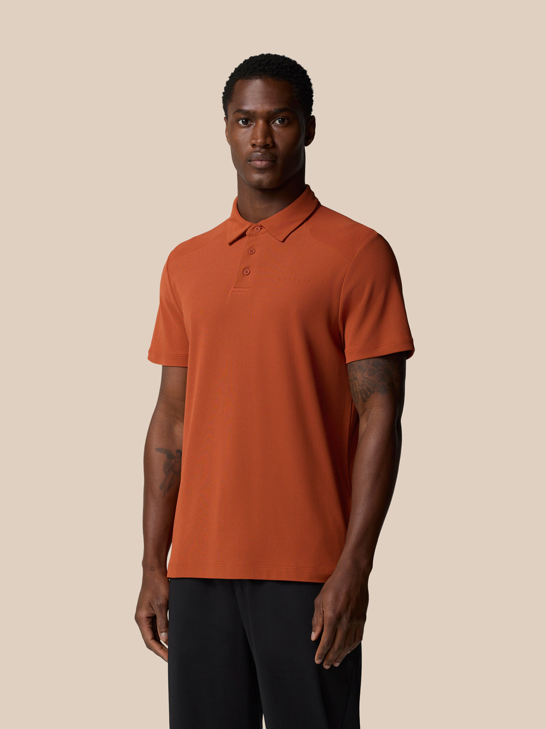 Front view of a man wearing a dark rust Elevated Lifestyle Polo Top with a left chest logo against a beige backdrop.