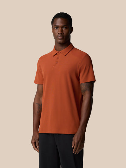 Front view of a man wearing a dark rust Elevated Lifestyle Polo Top with a left chest logo against a beige backdrop.