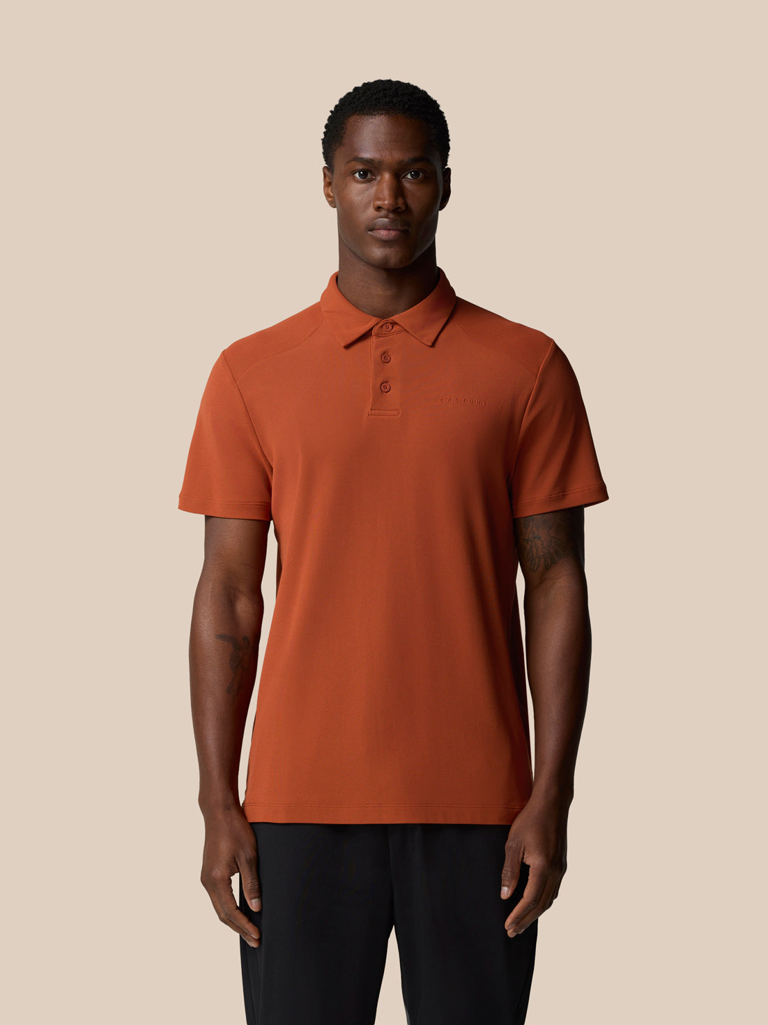 Rust polo shirt worn by a model with a collar and Castore wordmark on the left chest