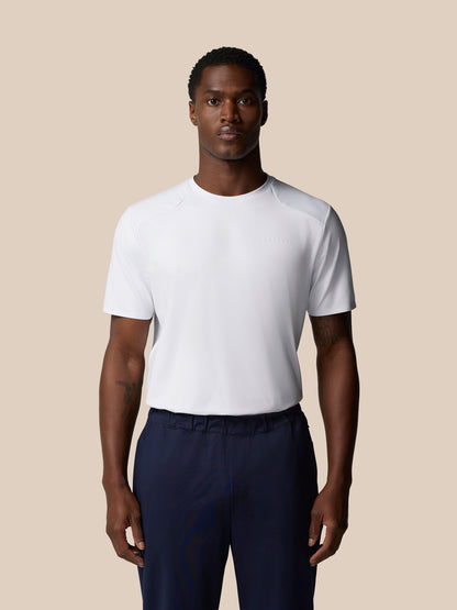 Male model wearing white Elevated Lifestyle T-Shirt with Castore wordmark on chest and navy pants against a beige backdrop.