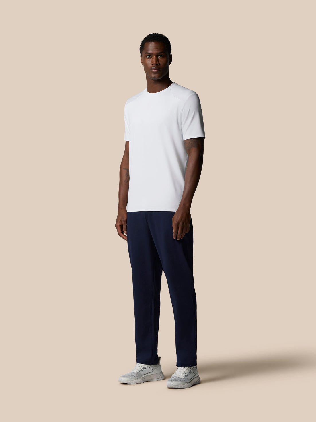 Male model in white Elevated Lifestyle T-Shirt and navy pants against a beige backdrop.