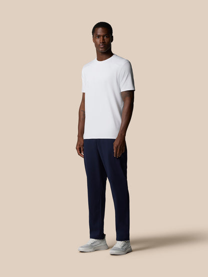 Male model in white Elevated Lifestyle T-Shirt and navy pants against a beige backdrop.
