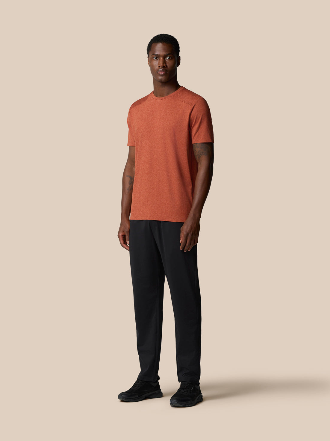 Three quarter view of rust elevated lifestyle T shirt on male model with visible left chest logo and back badge