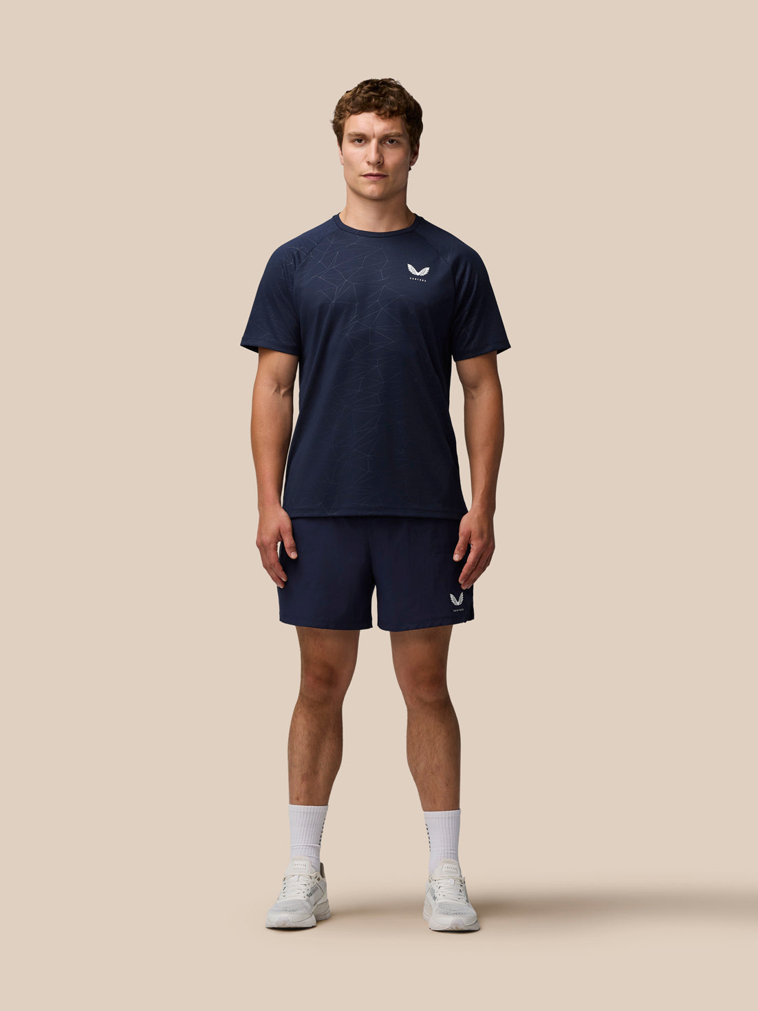 Full body shot of male model in navy Adapt All Over Print Short Sleeve T Shirt with geometric pattern and Castore logo on left chest