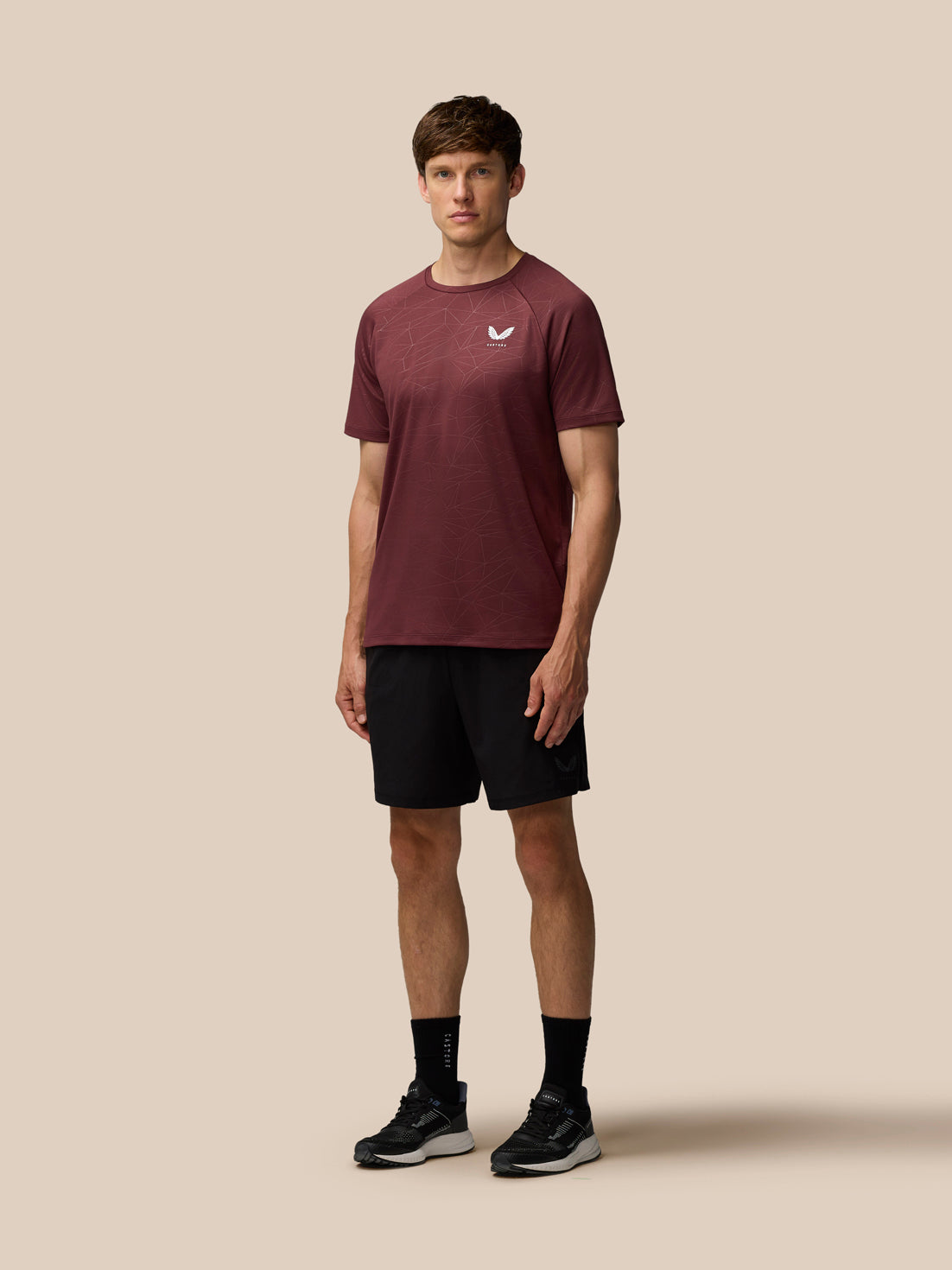 Front view of a man wearing plum Adapt Training T-Shirt with geometric print and Castore logo on the chest paired with black shorts