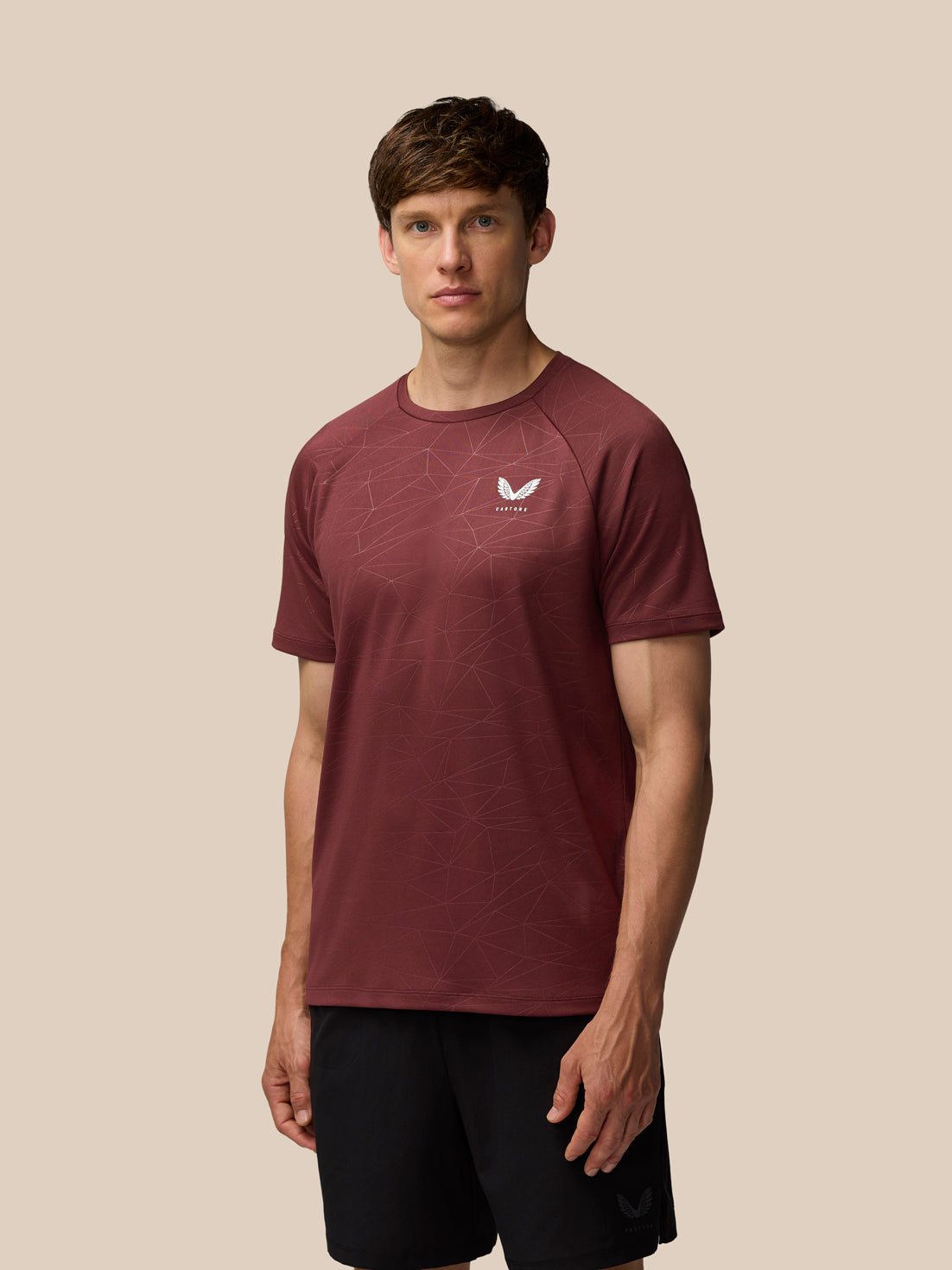 Male model in plum Adapt All Over Print Short Sleeve T-Shirt with geometric pattern against beige backdrop.