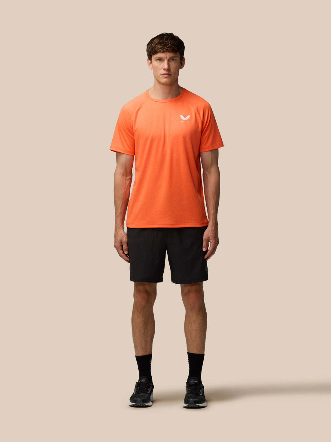Male model wearing bright orange Adapt Training T-Shirt with white Castore logo on the chest and a subtle geometric print.