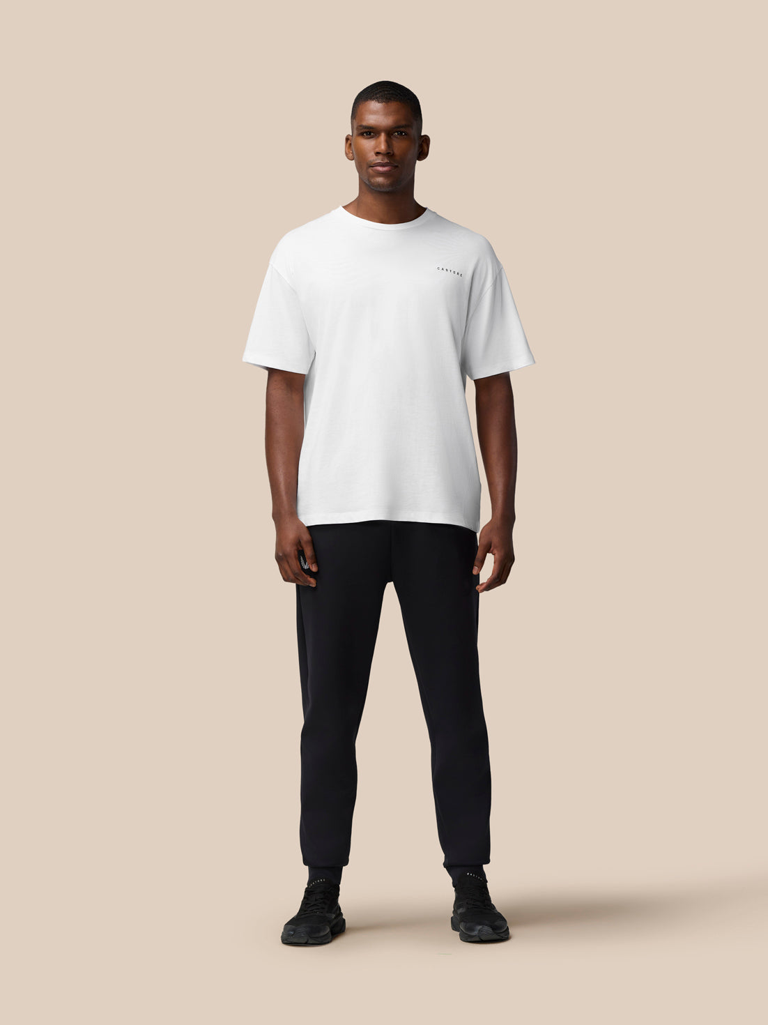 Male model wearing white Flex Cotton T Shirt with round neckline and relaxed fit against a beige backdrop