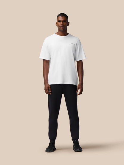 Male model wearing white Flex Cotton T Shirt with round neckline and relaxed fit against a beige backdrop