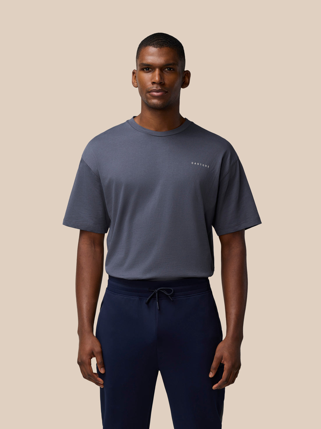 Male model in a pewter gray CASTORE T shirt with a small chest logo paired with navy drawstring shorts
