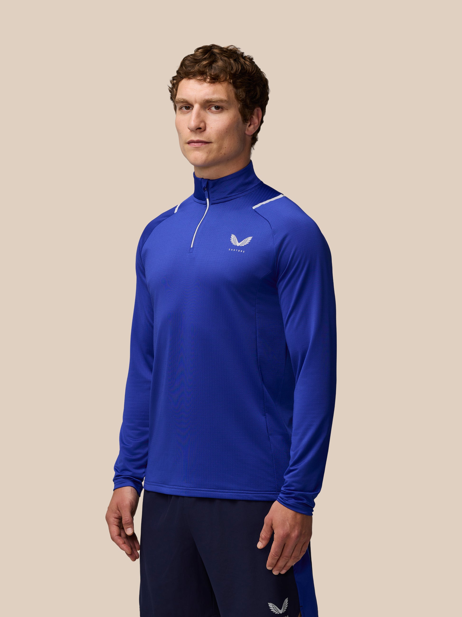 Male model wearing blue Apex Training Winterised 1/4 Zip Top with high collar and white seam detailing