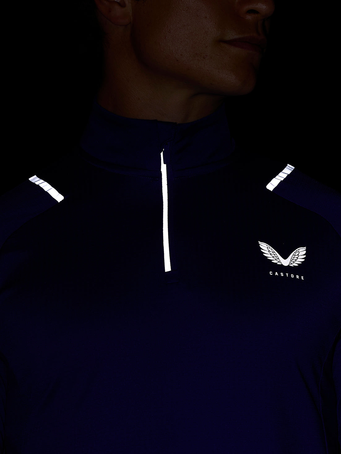 Close up of a model wearing navy Apex Training Winterised quarter-zip top with a white vertical zipper reflective shoulder detailing and the Castore wing logo on the chest