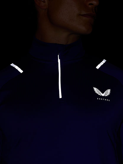 Close up of a model wearing navy Apex Training Winterised quarter-zip top with a white vertical zipper reflective shoulder detailing and the Castore wing logo on the chest