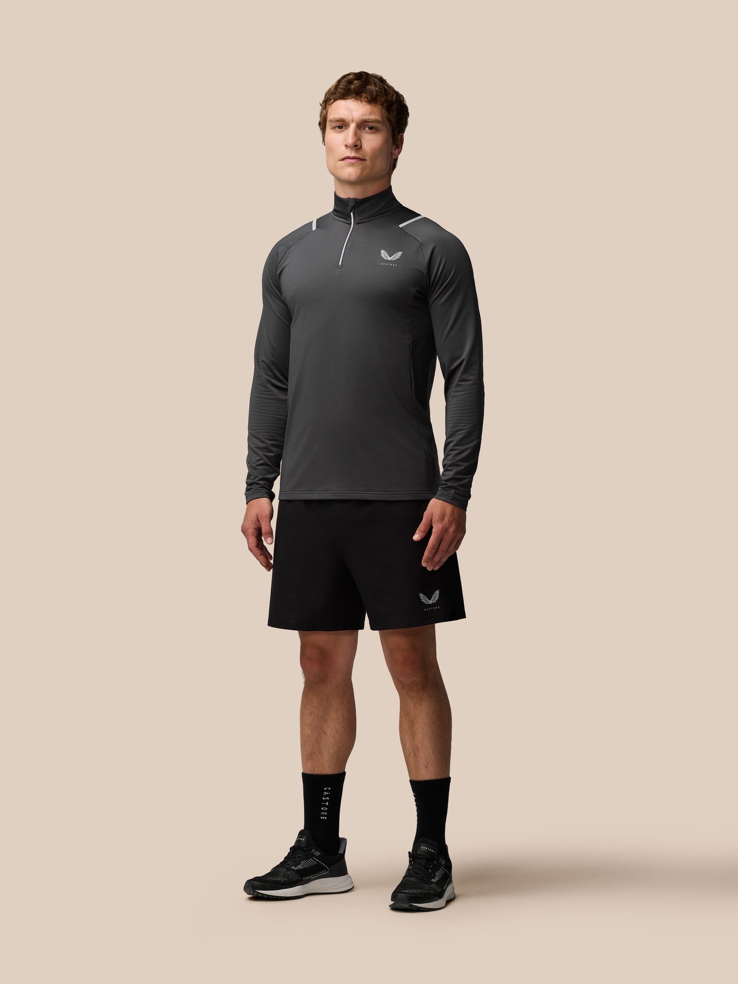 Male model wearing charcoal Apex Training Winterised quarter-zip top with high collar and subtle reflective piping.