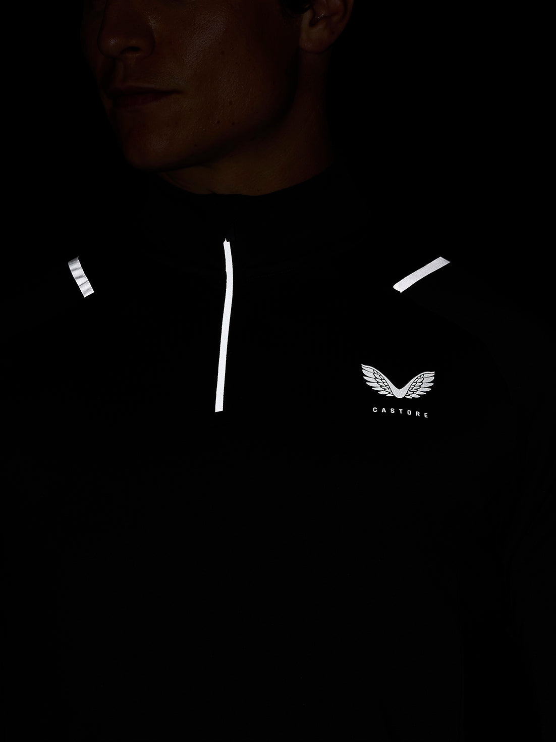 Close-up of a person wearing a black Apex Training Winterised ¼ Zip Top with reflective stripes and Castore wing logo on the chest
