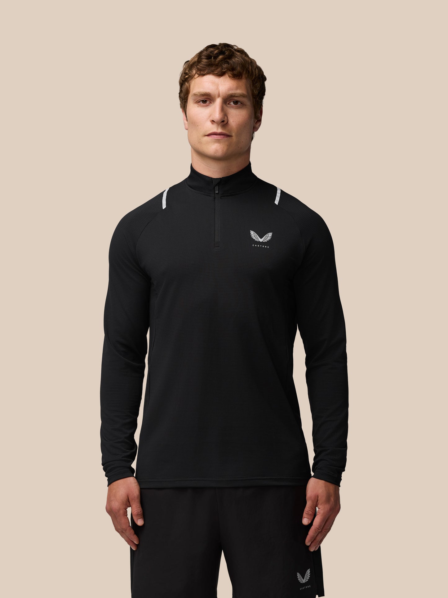 Front view of a man in a black Apex Training quarter zip top with reflective shoulder accents