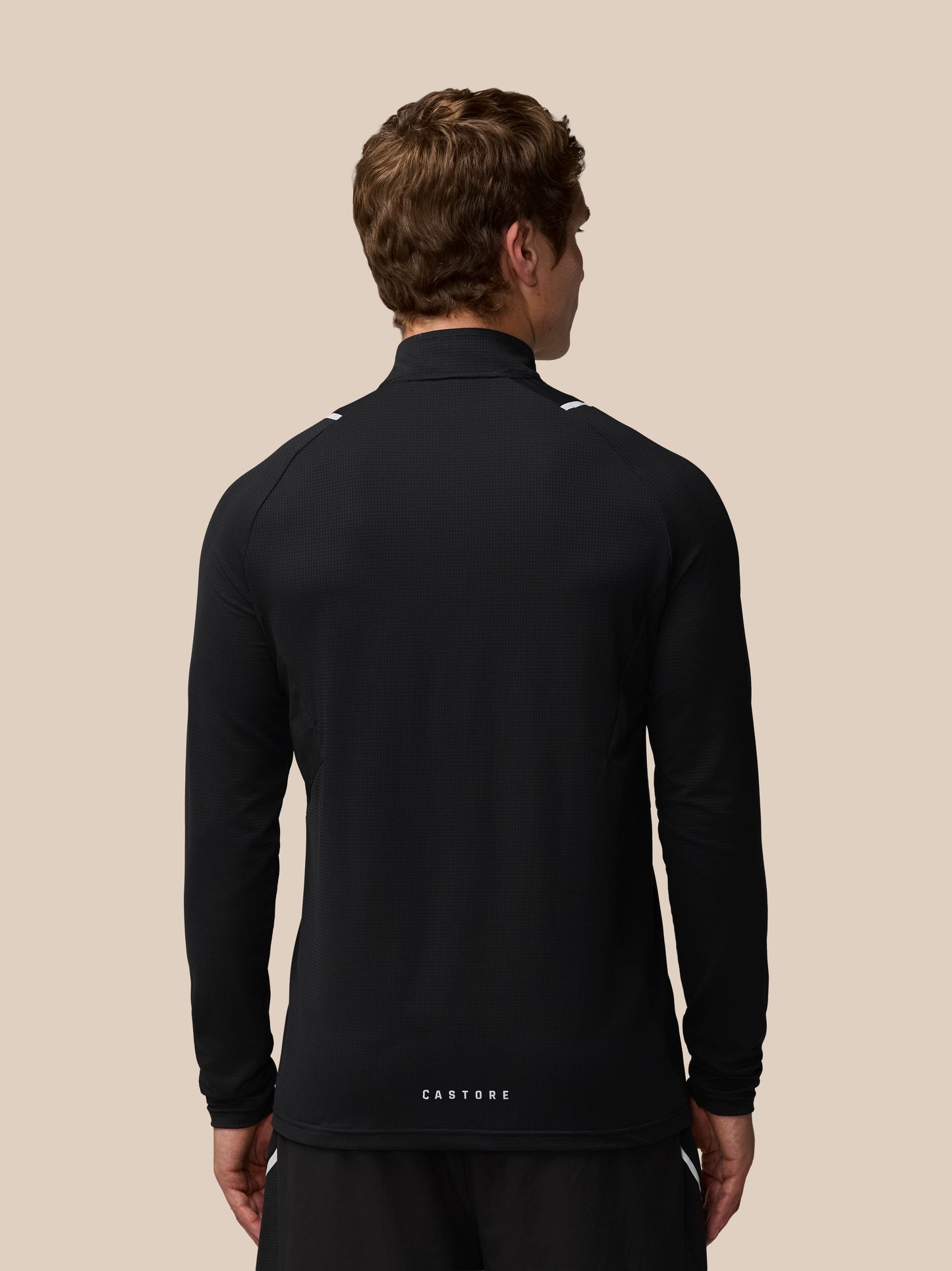 Back view of a man in black Apex Training quarter zip top with reflective shoulder highlights