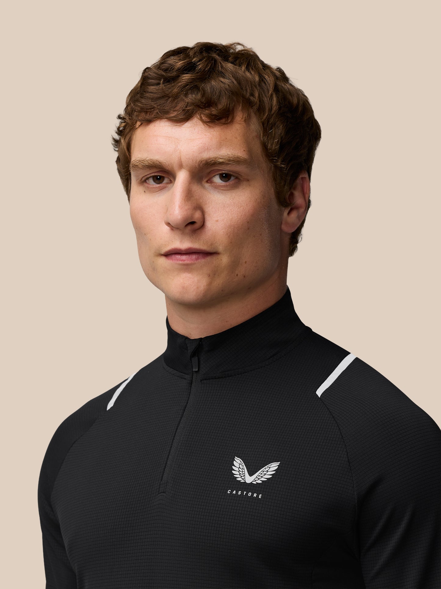 Head and shoulders of a man in black Apex Training 1/4 Zip Top with silver reflective shoulder hits and Castore chest logo