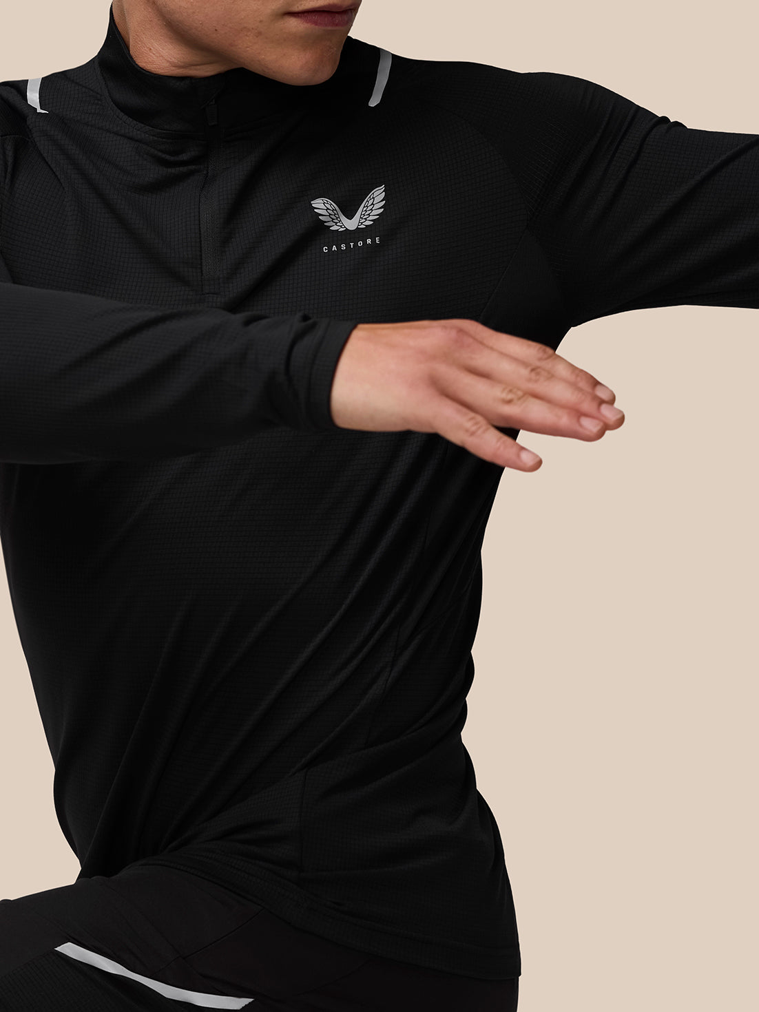 Close up of model in black Apex quarter zip with Castore logo on chest and reflective shoulder trim