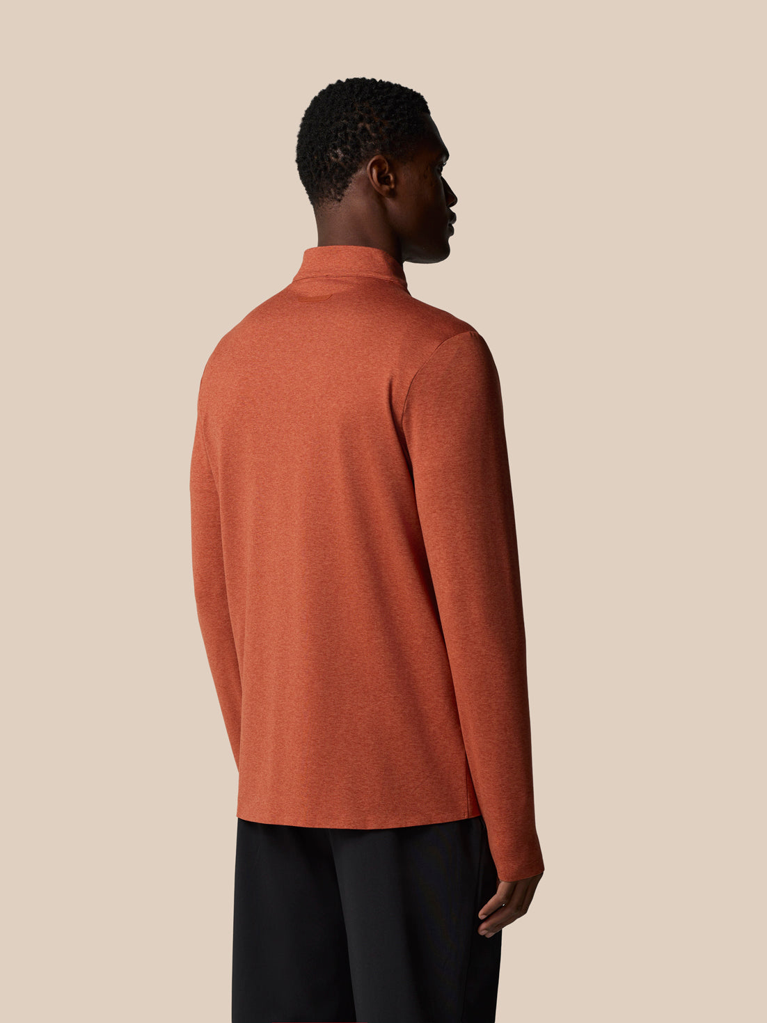 Back view of dark rust elevated lifestyle quarter zip top on a male model showing back neck tape and Castore badge