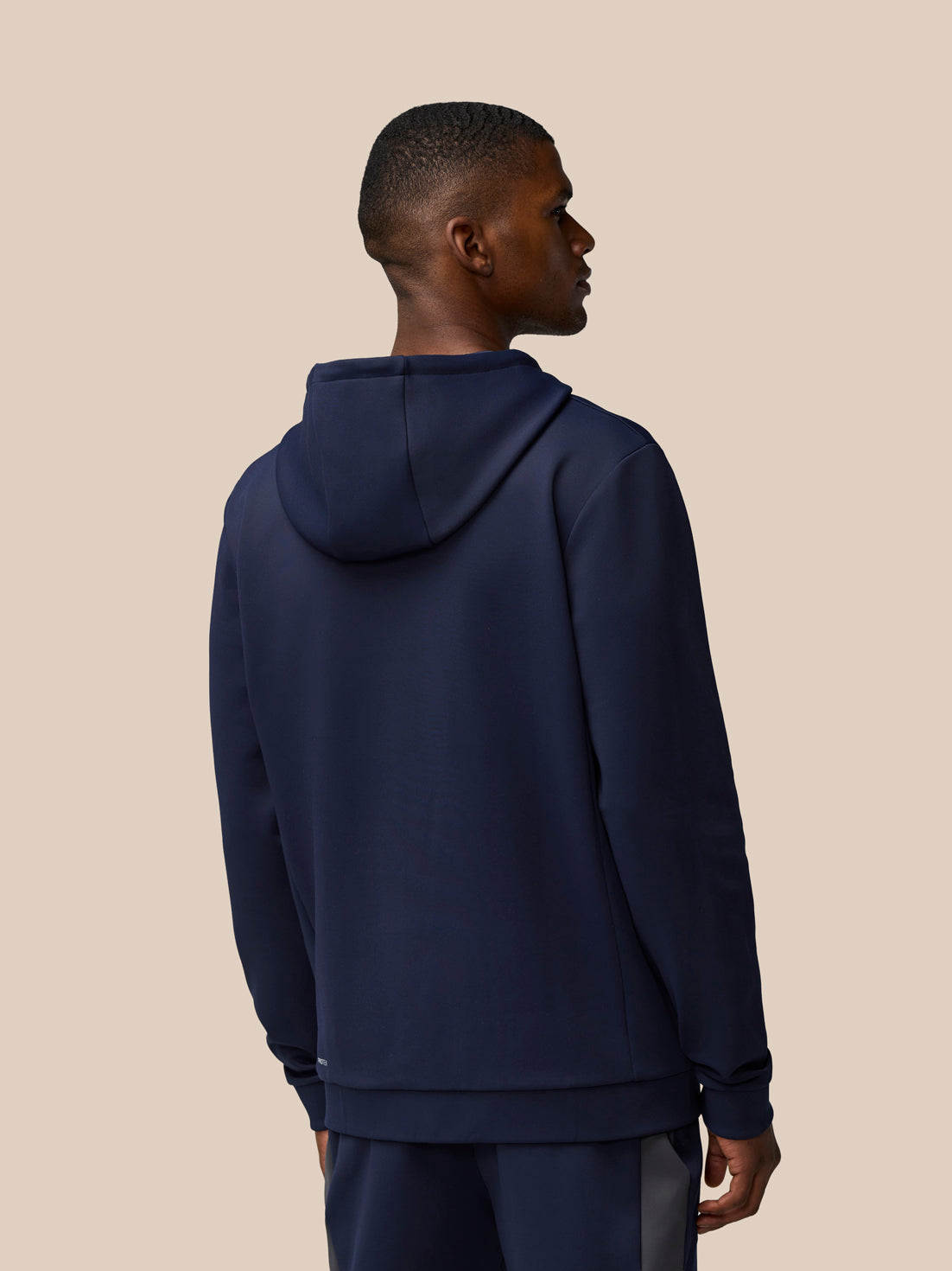 Back view of a model wearing a navy Flex Lifestyle Thermo Hoodie with hood down against a beige background