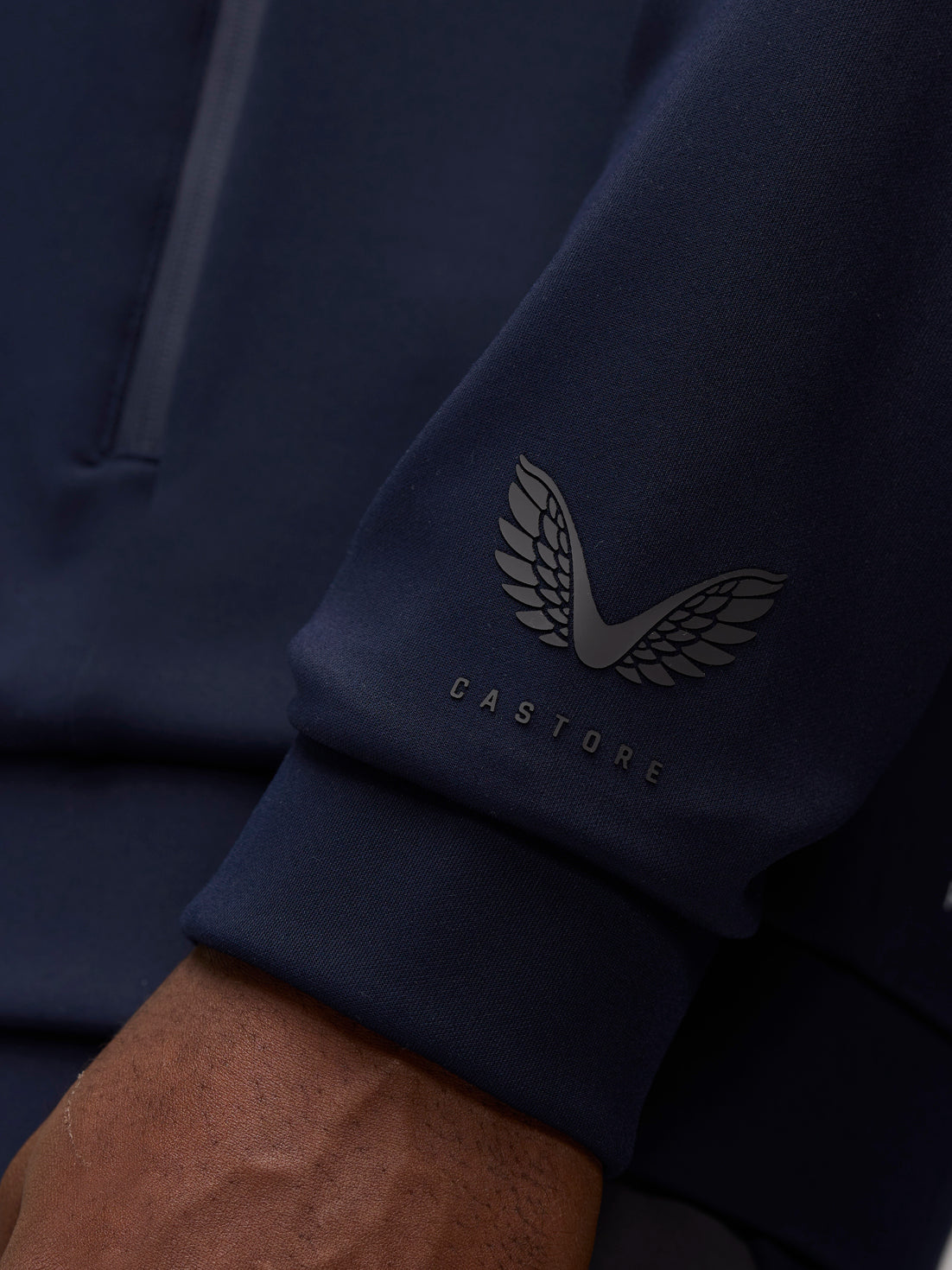 Close-up of navy sleeve showing Castore wing logo and wordmark near the cuff.