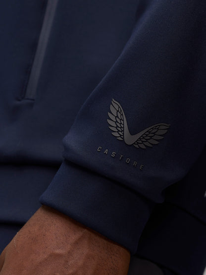 Close-up of navy sleeve showing Castore wing logo and wordmark near the cuff.