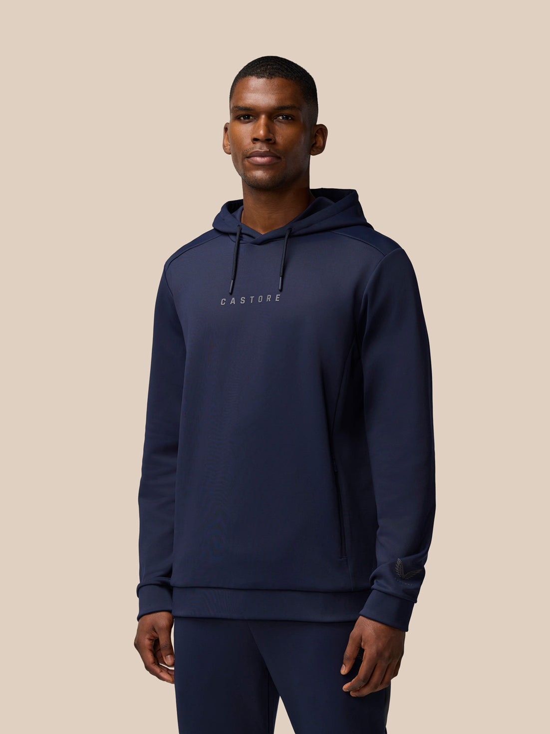 Male model wearing navy Flex Thermo Long Sleeve Hoodie with hood and Castore wordmark at center chest
