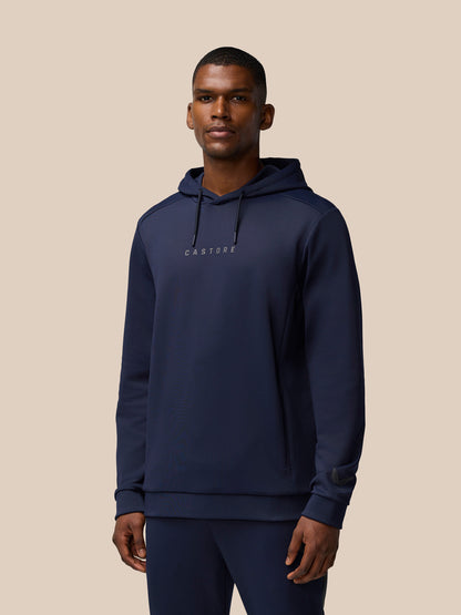 Male model wearing navy Flex Thermo Long Sleeve Hoodie with hood and Castore wordmark at center chest