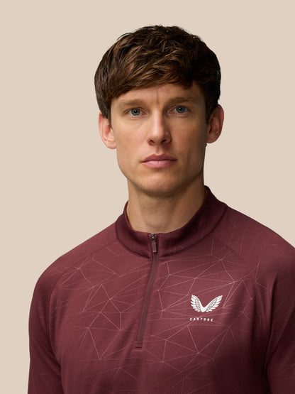 Close-up of male model wearing plum quarter-zip training top with geometric line pattern and Castore logo on chest.