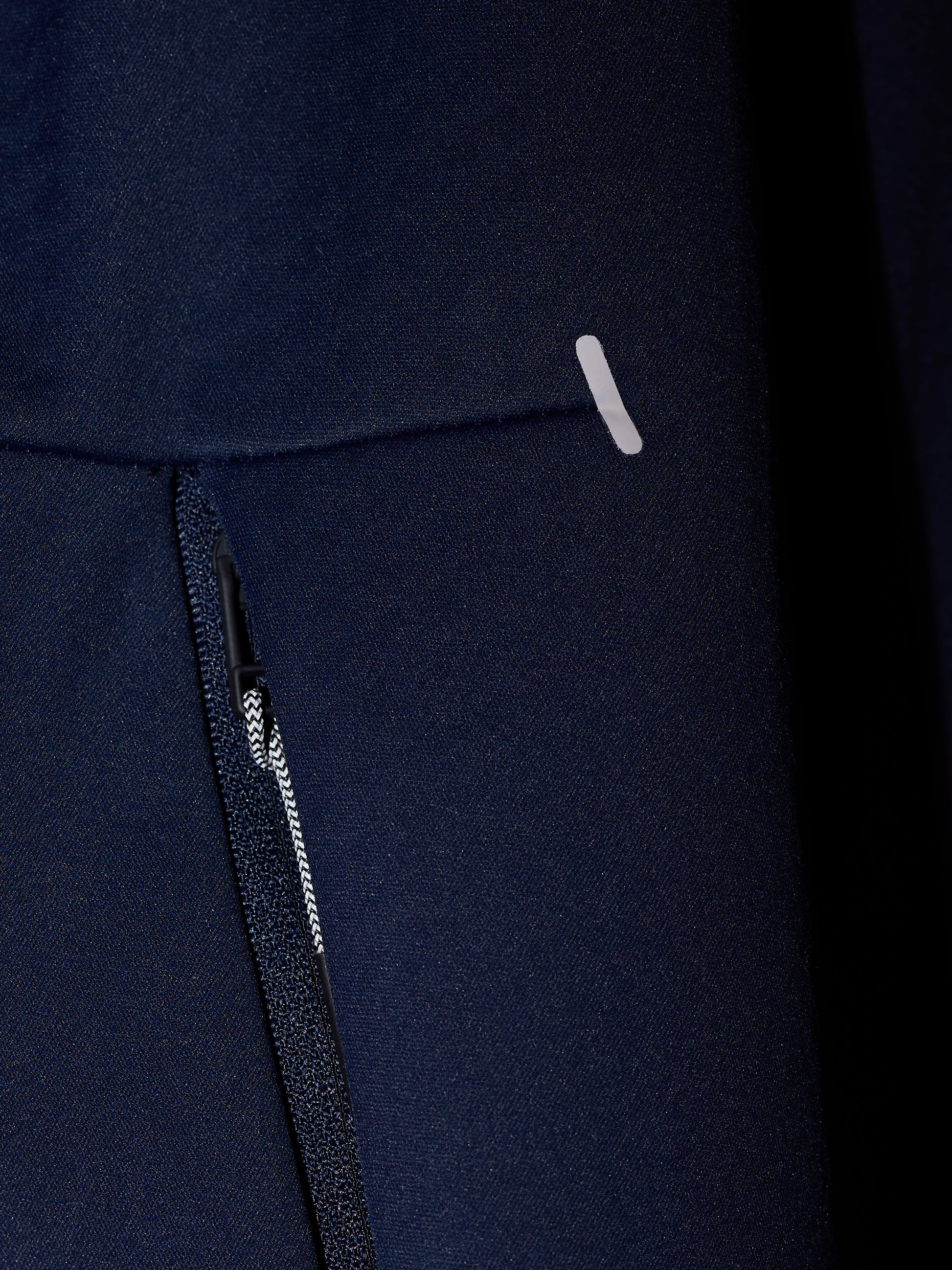 Close-up of navy Garcia 3.0 Hoodie fabric showing a zipper and small reflective tab.