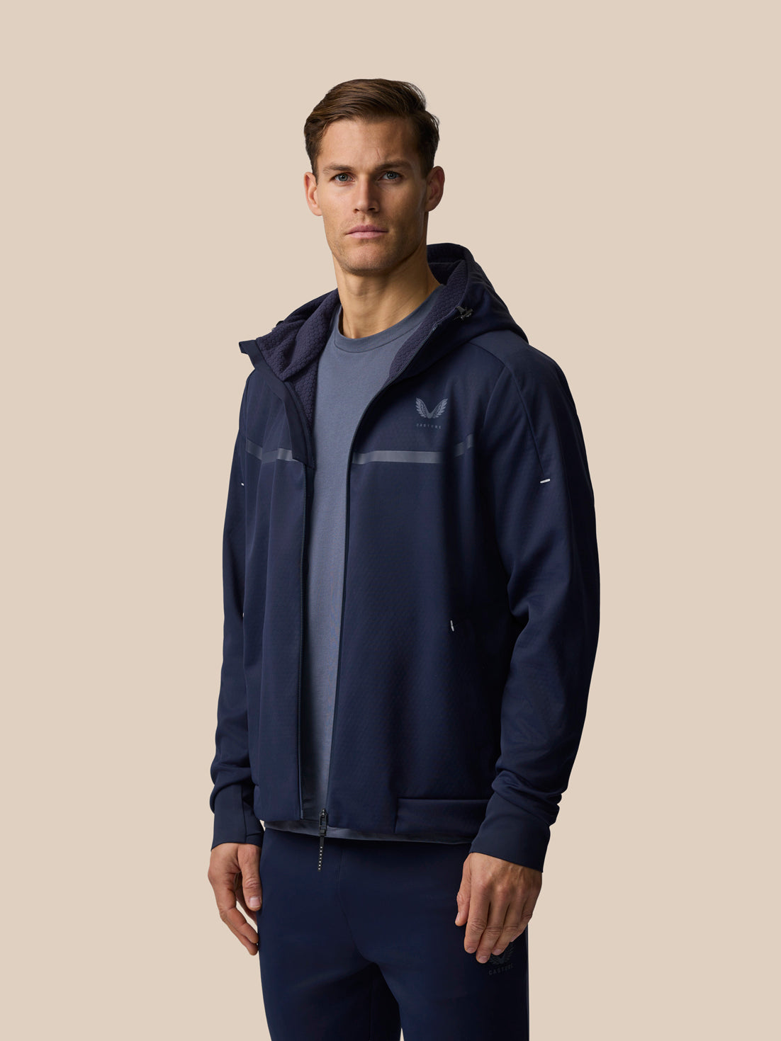 Three-quarter front view of man wearing navy Garcia 3.0 Hoodie with hood down, reflective chest stripe, and logo.