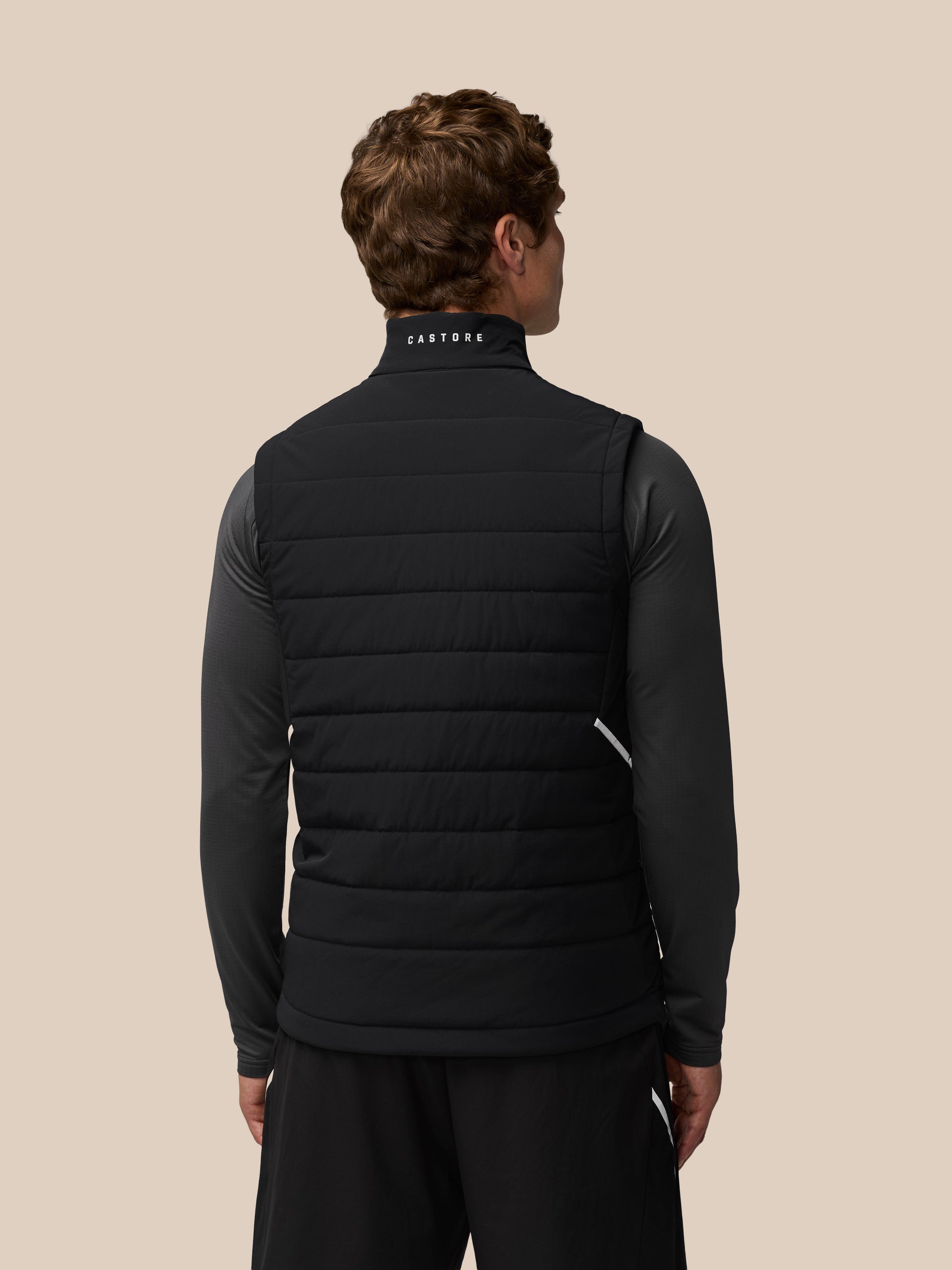 Back view of a man in a black Apex Training Gilet with Castore wordmark on the back collar