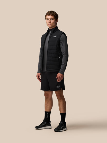 Man wearing black Apex Training Gilet over a gray top, posing against beige background.