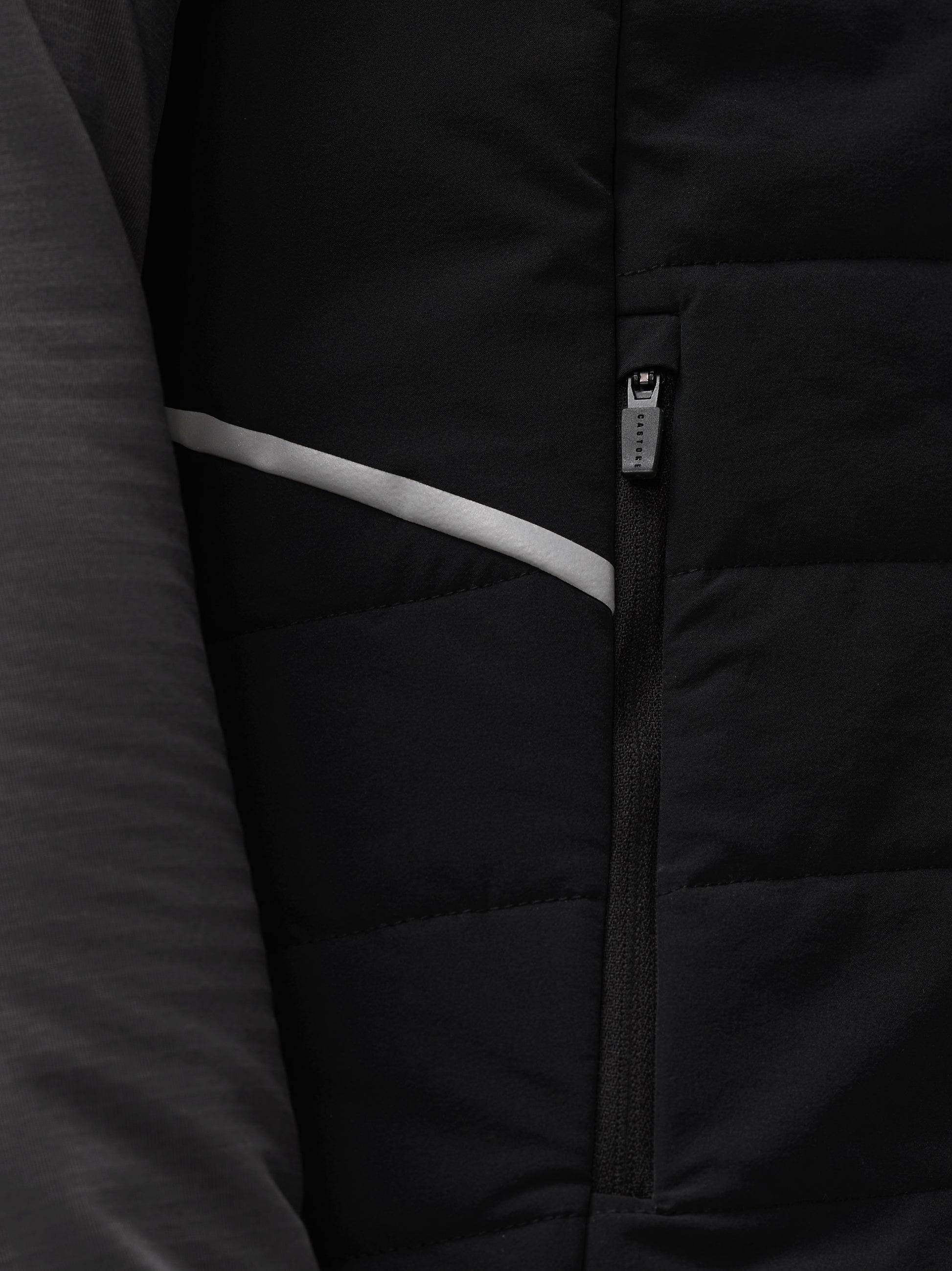 Close up detail of black padded Apex Gilet zipper with Castore branding and a light reflective stripe