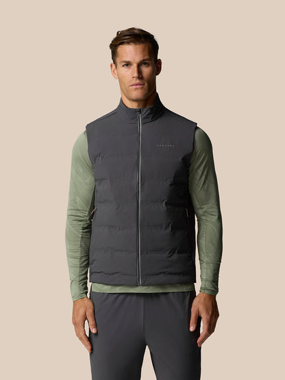 Male model wearing Zone Training LVS Insulated Gilet in gunmetal over olive long sleeve, with front zipper and sleeveless design.