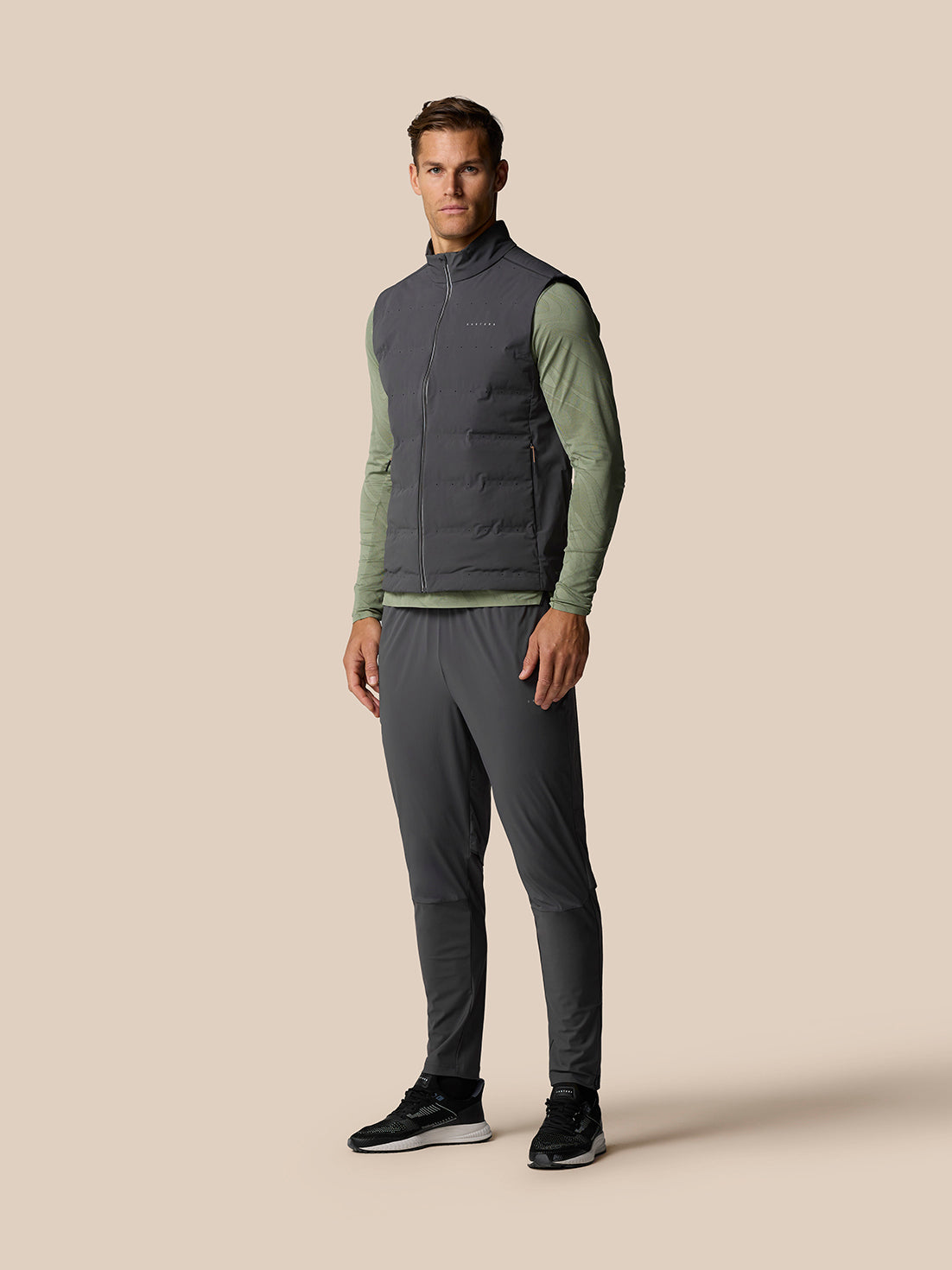 Male model wearing Zone Training LVS Insulated Gilet in gunmetal over olive green long sleeve top, full body shot