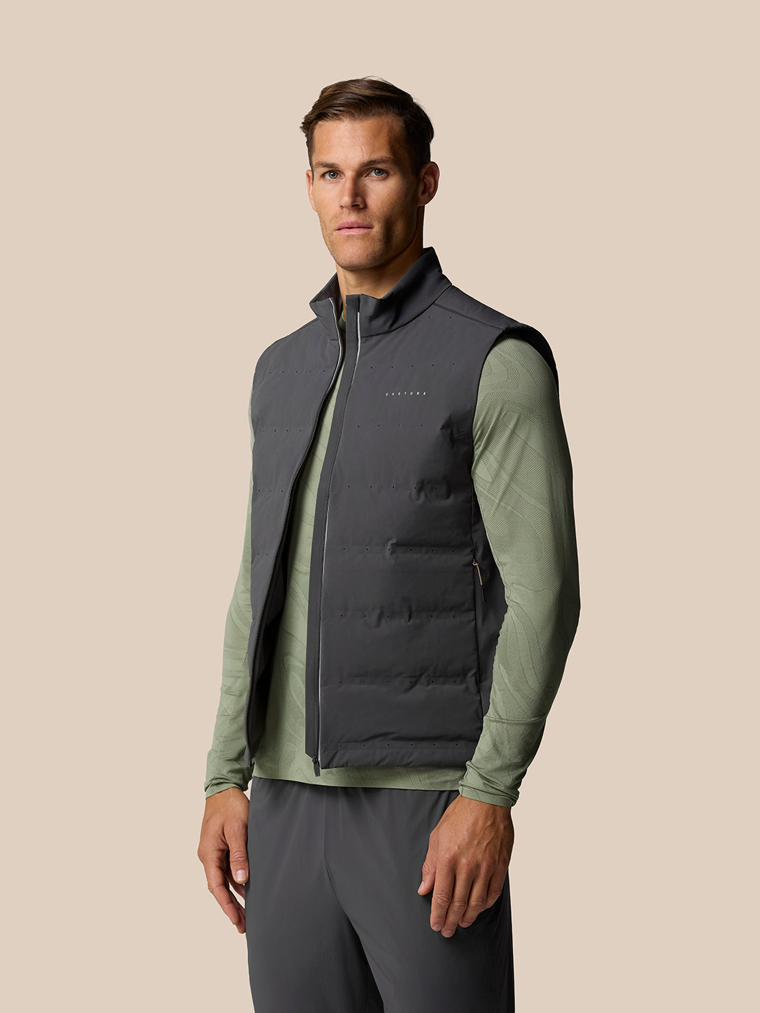 Male model wearing Zone Training LVS Insulated Gilet in gunmetal with reflective accents over a green top, front view